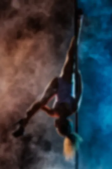 Upside down on the pole, one leg pointed skyward, through smoke that shifts from copper on one side to deep blue.